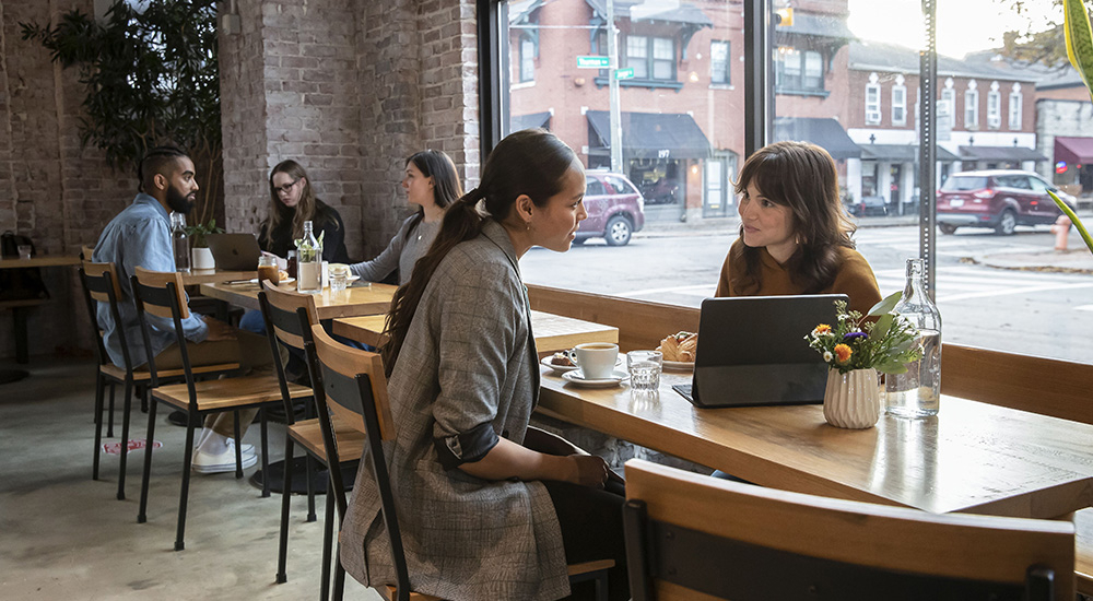 Dos mujeres en una cafetería hablando y mirando una tableta